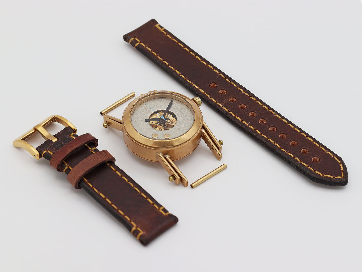 Deconstructed bronze watch with brown leather strap on a light gray background