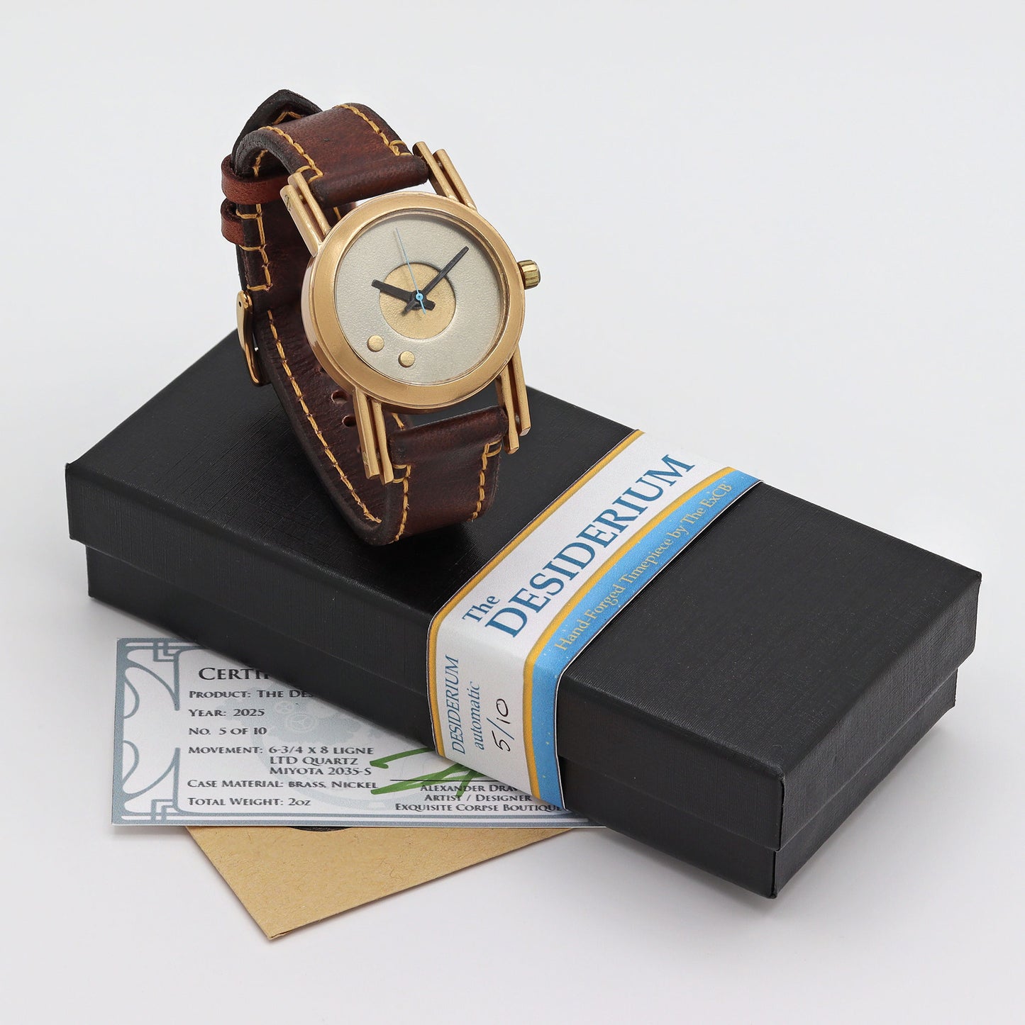 Gold watch with brown leather strap on a black box with 'Desiderium' label