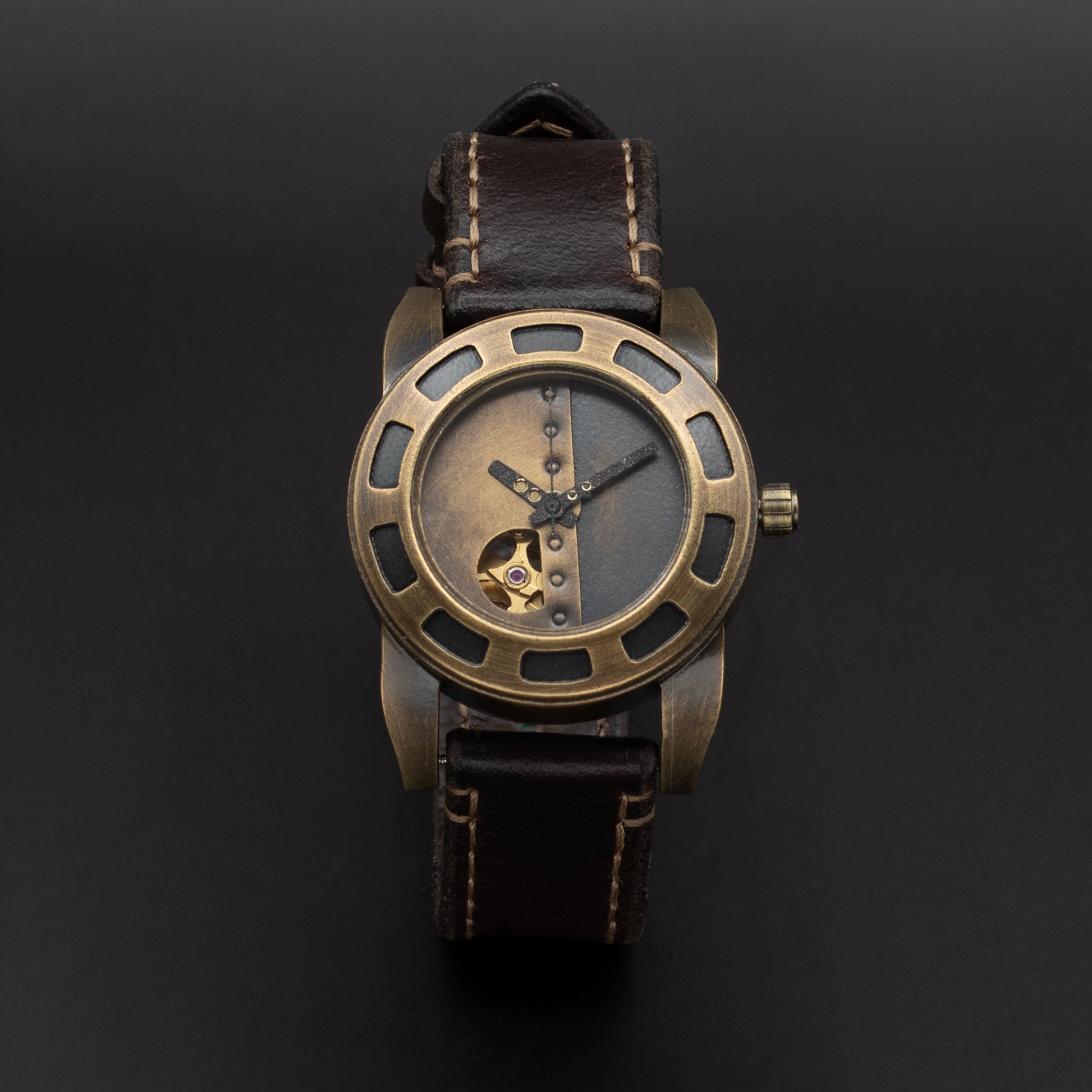 A vintage-style wristwatch with a bronze-toned metal case, skeleton dial showing a gold mechanical movement, and a dark brown leather strap with light stitching, set against a dark background.