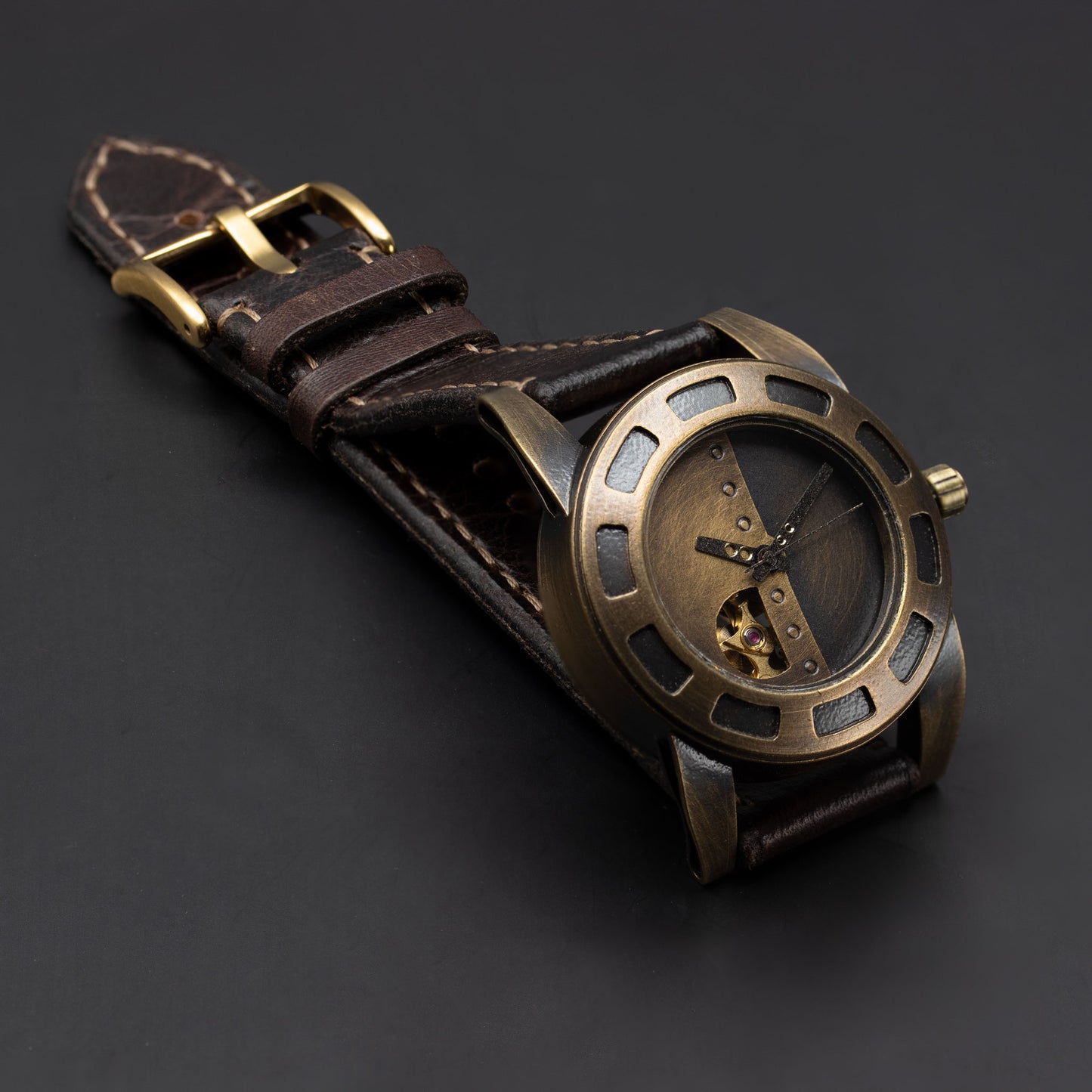 A steampunk-style wristwatch with an antique bronze-toned metal case, skeleton dial, and a dark brown leather strap, displayed on a dark gray background.