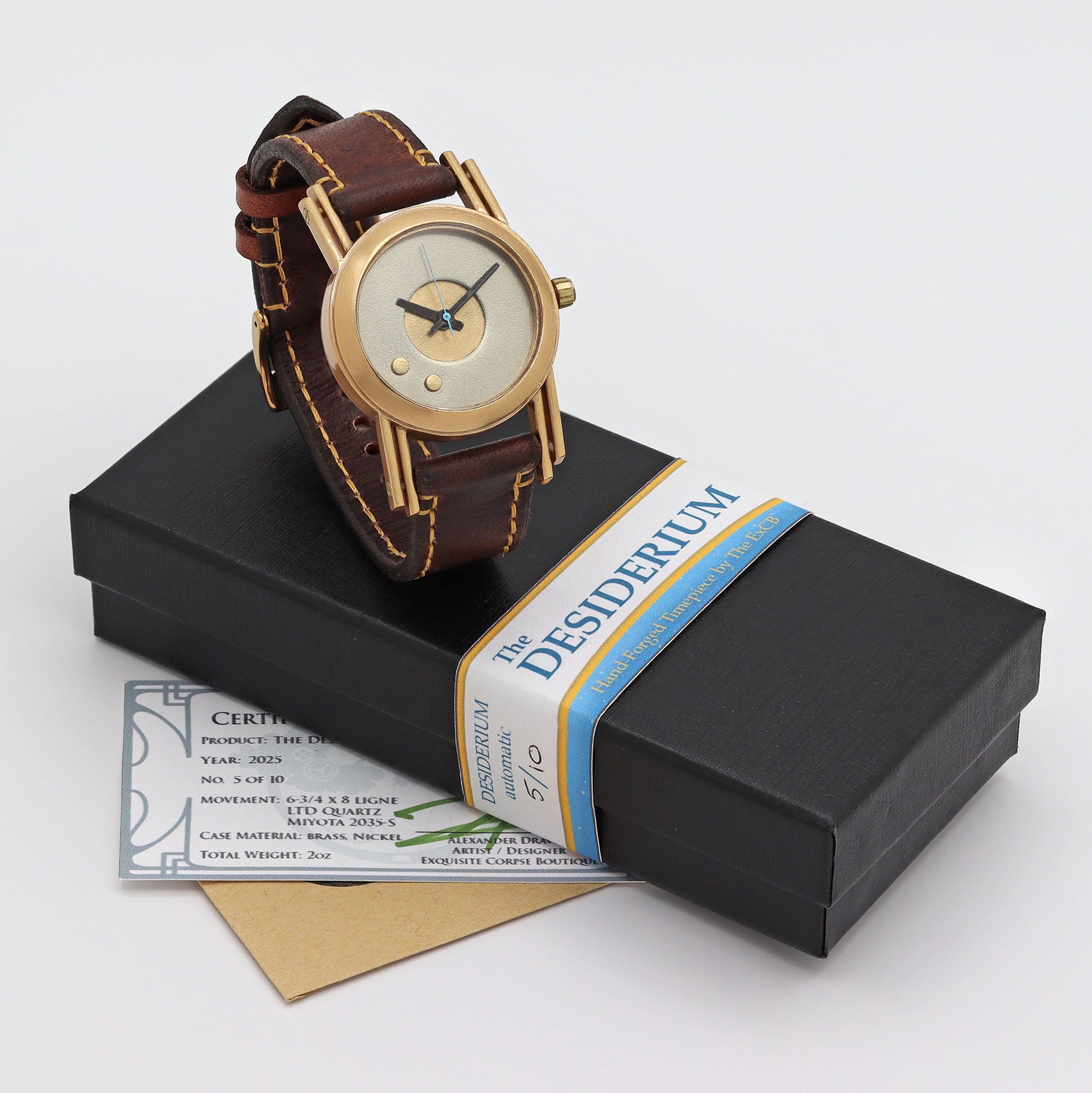 Gold watch with brown leather strap on a black box with 'Desiderium' label